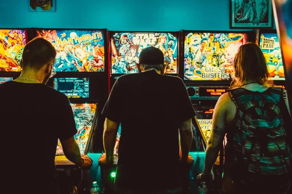 Trzy osoby grają w pinball w salonie gier