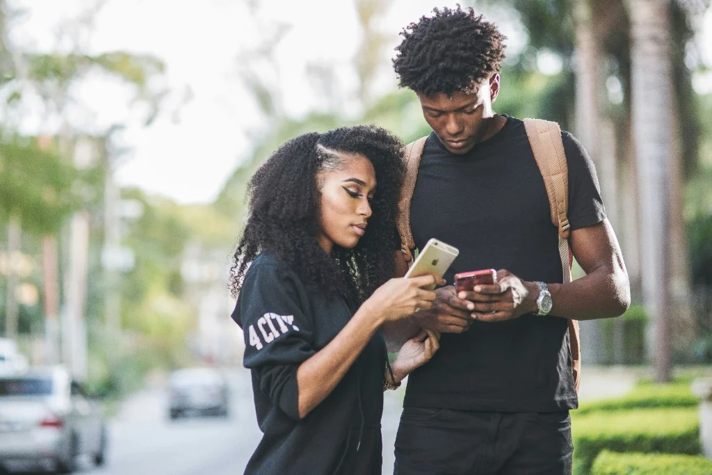 Two people side by side check their phones on a sunny street before a first date.