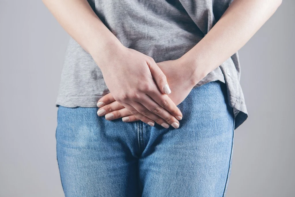 Person standing with hands folded protectively in front, a gesture of personal boundary on a neutral background.