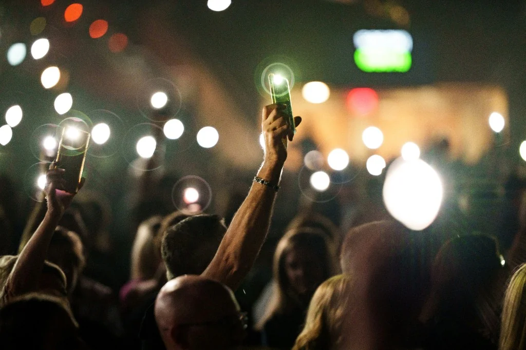 Night concert crowd holding up phones with lights glowing in the dark.