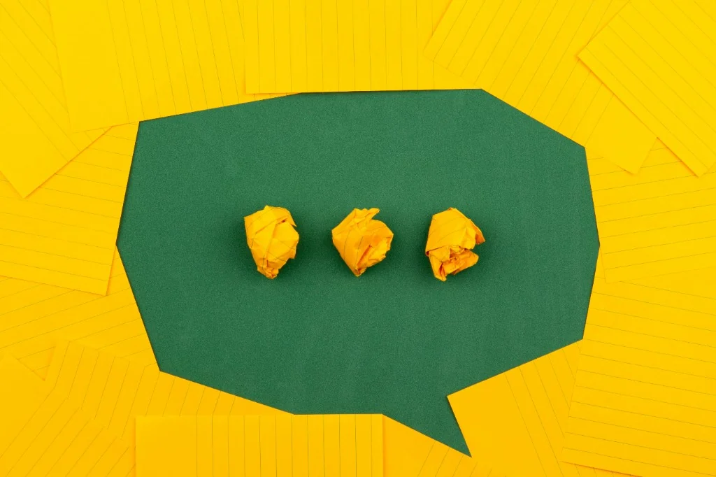 Yellow sticky notes forming a speech bubble on a green surface, with three paper balls—communication and taking a pause to respond.